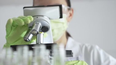 Bilimsel araştırma ve analizlerin önemini vurgulayarak bir laboratuvarda mikroskobu ayarlayan bir bilim adamının yeşil eldivenli ellerine yakın çekim. Tıp, sağlık ve bilim konsepti.