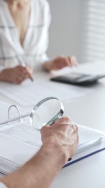 Profesyonel muhasebeciler, parlak ofislerindeki mali raporları denetlemek için bir büyüteç ve hesap makinesi kullanarak birlikte çalışıyorlar. Denetim ve vergi kavramı.