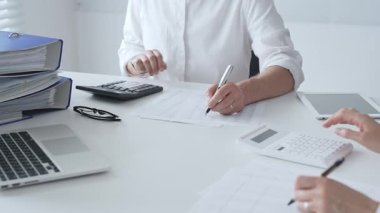 Finans uzmanları hesap tablolarını inceliyor, hesap makineleriyle modern çalışma alanında birlikte çalışıyor, raporları tartışıyorlar. Ticarette denetim ve vergiler.