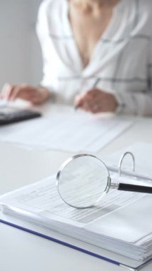 Büyüteç finansal belgelerde, hesap makinesi kullanan ve not alan bir muhasebeciyle birlikte dikey görüşü kapatıyor. Ticarette denetim ve vergiler.