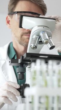 Koruyucu ekipman araştırmacısı steril bir laboratuvar ortamında mikroskopla numuneleri analiz ediyor. Tıp, sağlık ve bilim konsepti.