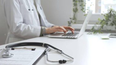 Stetoskop ve tıbbi kayıtlar doktorun karşısındaki masada. Bilgisayarında tıbbi bir büro var. İnternet üzerinden sağlık hizmeti ya da teletıp hizmeti sunuyor. Tıp konsepti.