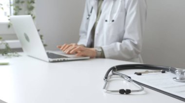 Stetoskop ve tıbbi kayıtlar doktorun karşısındaki masada. Bilgisayarında tıbbi bir büro var. İnternet üzerinden sağlık hizmeti ya da teletıp hizmeti sunuyor. Tıp konsepti.