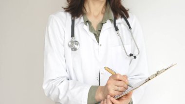 Yeşil bir bluzun üzerine steteskop ve sağlık önlüğü giyen kimliği belirsiz kadın doktor, beyaz bir panoya tıbbi uzmanlığı ve hasta bakımını temsil eden bir yazı yazıyor. Tıp konsepti.