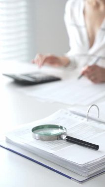 Büyüteç finansal belgelerde, hesap makinesi kullanan ve not alan bir muhasebeciyle birlikte dikey görüşü kapatıyor. Ticarette denetim ve vergiler.