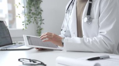 Tablet üzerindeki hasta verilerini inceleyen, çağdaş klinik ortamlarda beyaz laboratuvar önlüğü ve steteskop giyen, dijital sağlık danışmanlığı yapan bir tıp uzmanı. İlaç ve sağlık hizmetleri