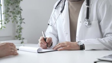 Doktor, parlak ve modern bir klinikteki muayene sırasında hasta sağlığıyla ilgili endişeleri dinliyor ve reçete yazıyor. İlaç ve sağlık hizmetleri kavramı.