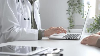 Klinik ortamdaki sağlık hizmetleri sırasında hasta bilgilerini, laptopunu ve steteskopunu kayıt altına alan beyaz önlüklü bir tıbbi uzman. İlaç ve sağlık hizmetleri kavramı