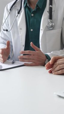 Doktor adam yeşil gömleğin üstüne sağlık önlüğü giyiyor ve steteskop klinikteki muayene sırasında hastaya teşhisi açıklarken elleriyle işaret ediyor. İlaç ve sağlık hizmetleri