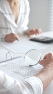 Profesyonel muhasebeciler, parlak ofislerindeki mali raporları denetlemek için bir büyüteç ve hesap makinesi kullanarak birlikte çalışıyorlar. Denetim ve vergi kavramı.