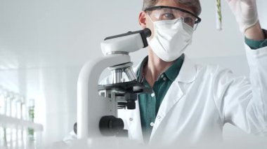 Biyolojik analiz sırasında steril bir laboratuvarda yeşil botanik örneklerini inceleyen maskeli yetişkin bir araştırmacı. Tıp, sağlık ve bilim konsepti.