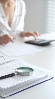 Büyüteç finansal belgelerde, hesap makinesi kullanan ve not alan bir muhasebeciyle birlikte dikey görüşü kapatıyor. Ticarette denetim ve vergiler.