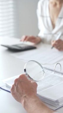 Profesyonel muhasebeciler, parlak ofislerindeki mali raporları denetlemek için bir büyüteç ve hesap makinesi kullanarak birlikte çalışıyorlar. Denetim ve vergi kavramı.