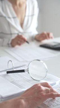 Hesap makinesi kullanan ve notlar alan bir muhasebecinin muhasebe, finans ve vergi hazırlıklarını vurguladığı mali belgelerde büyüteç kapat. Ticarette denetim ve vergiler.