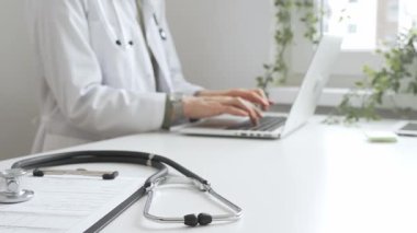 Stetoskop ve tıbbi kayıtlar doktorun karşısındaki masada. Bilgisayarında tıbbi bir büro var. İnternet üzerinden sağlık hizmeti ya da teletıp hizmeti sunuyor. Tıp konsepti.