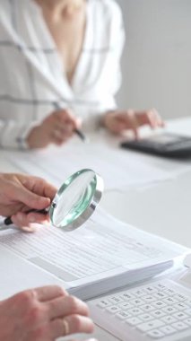 Profesyonel muhasebecilerden oluşan bir ekip, bir büyüteç ve hesap makinesi kullanarak, parlak ofislerindeki mali raporları denetlemek için birlikte çalışıyorlar. Ticarette denetim ve vergiler.