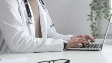 Laptop üzerinde çalışan, modern, iyi aydınlatılmış sağlık ortamında beyaz önlük ve steteskop giyen, klinik uzmanlığı dijital teknolojiyle harmanlayan bir tıp uzmanı. İlaç ve sağlık hizmetleri