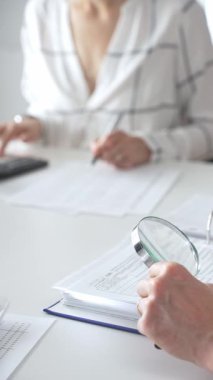 Profesyonel muhasebecilerden oluşan bir ekip, bir büyüteç ve hesap makinesi kullanarak, parlak ofislerindeki mali raporları denetlemek için birlikte çalışıyorlar. Ticarette denetim ve vergiler.