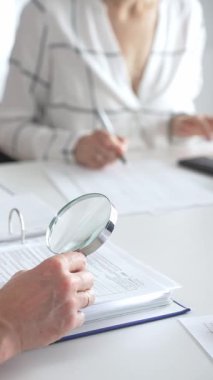 Profesyonel muhasebeciler, parlak ofislerindeki mali raporları denetlemek için bir büyüteç ve hesap makinesi kullanarak birlikte çalışıyorlar. Denetim ve vergi kavramı.