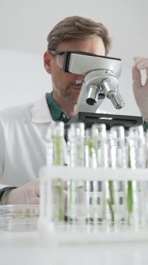 Beyaz koruyucu giysiler içinde erkek bilim araştırmacısı steril bir laboratuvar ortamında mikroskopla numuneleri analiz ediyor. Tıp, sağlık ve bilim konsepti.