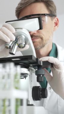 Koruyucu ekipman araştırmacısı steril bir laboratuvar ortamında mikroskopla numuneleri analiz ediyor. Tıp, sağlık ve bilim konsepti.