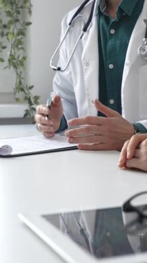 Doktor adam yeşil gömleğin üstüne sağlık önlüğü giyiyor ve steteskop klinikteki muayene sırasında hastaya teşhisi açıklarken elleriyle işaret ediyor. İlaç ve sağlık hizmetleri