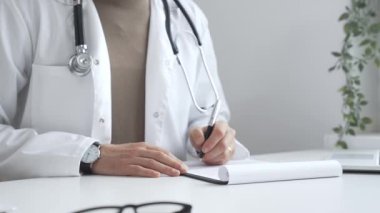 Laboratuvar önlüğü ve steteskop giyen doktor tıbbi reçete yazıyor ya da ofis masasında oturan tıbbi belgeleri dolduruyor. İlaç ve sağlık hizmetleri