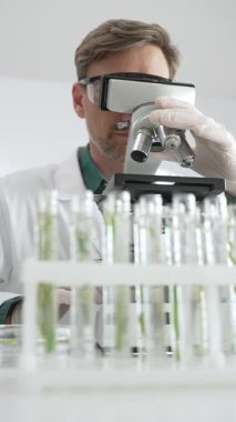 Korumalı teçhizat araştırmacısı steril bir laboratuvar ortamında mikroskopla numuneleri analiz ediyor. Tıp, sağlık ve bilim konsepti.