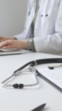 Stetoskop ve tıbbi kayıtlar doktorun karşısındaki masada. Bilgisayarında tıbbi bir büro var. İnternet üzerinden sağlık hizmeti ya da teletıp hizmeti sunuyor. Tıp konsepti.