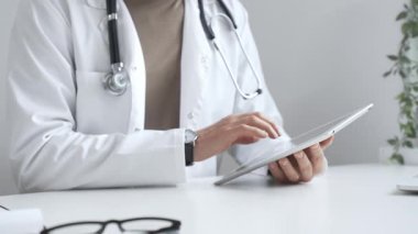 Tablet üzerindeki hasta verilerini inceleyen, çağdaş klinik ortamlarda beyaz laboratuvar önlüğü ve steteskop giyen, dijital sağlık danışmanlığı yapan bir tıp uzmanı. İlaç ve sağlık hizmetleri