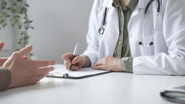 Doktor kadın, erkek hasta sağlığıyla ilgili endişeleri dinliyor ve parlak, modern bir klinikteki muayenede reçete yazıyor. Kapatın. İlaç ve sağlık hizmetleri kavramı.