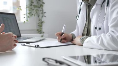 Doktor kadın, erkek hasta sağlığıyla ilgili endişeleri dinliyor ve parlak, modern bir klinikteki muayenede reçete yazıyor. Kapatın. İlaç ve sağlık hizmetleri kavramı.