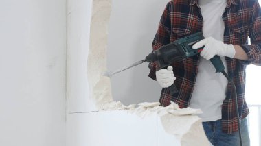 Kırmızı kareli kotlar ve koruyucu eldivenler giyen kimliği belirsiz erkek inşaat işçilerinin yakın çekiç matkabıyla beyaz duvarı yıkıp toz oluşturuyor. Yenileme konsepti.