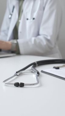 Stetoskop ve tıbbi kayıtlar doktorun karşısındaki masada. Bilgisayarında tıbbi bir büro var. İnternet üzerinden sağlık hizmeti ya da teletıp hizmeti sunuyor. Tıp konsepti.
