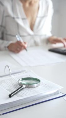 Büyüteç finansal belgelerde, hesap makinesi kullanan ve not alan bir muhasebeciyle birlikte dikey görüşü kapatıyor. Ticarette denetim ve vergiler.