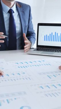 Masada oturan işadamı, mali verileri tartışırken mali tablolara, iş arkadaşlarıyla ofis toplantılarında pazar eğilimlerini işaret ediyor. İş adamları konsepti.