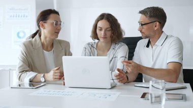 Professional team reviewing project data on laptop, working together in modern office environment, collaborating with focused corporate energy. Business people concept.