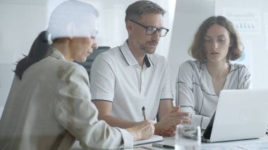 Business team collaborating on a project, analyzing data on a laptop, taking notes, and engaging in problem solving in a modern office environment