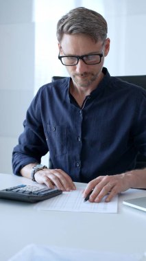 Professional businessman calculating financial data, reviewing documents near laptop in modern workplace setting. Audit and taxes, business concept