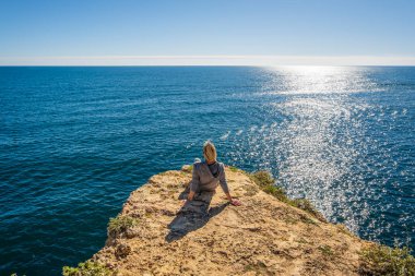 Portekiz 'in Algarve kentindeki Marinha Sahili' nde Atlantik Okyanusu 'nun güzelliğine dalmış, uçurumların tepesinde oturan genç bir kadının arkası.