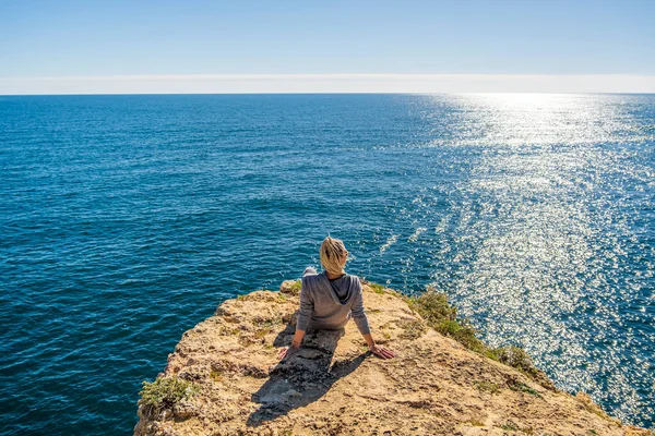 若い女性の背中の崖の上に座っているアルガルヴェのマリナビーチで大西洋の美しさに浸漬 ポルトガル — ストック写真