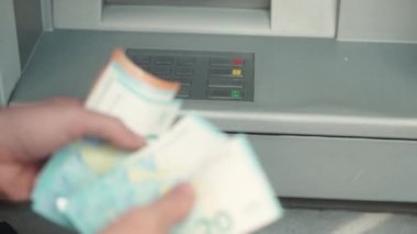 Extreme close-up of hands of adult caucasian businessman counting withdrawn euro notes. Young male holding money received from bank card using ATM terminal. Finance concept.