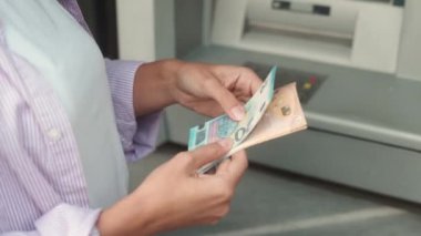 Extreme close-up of young woman withdrawing cash euro notes from ATM terminal. Caucasian female counting bills received from debit card standing on street. Financial operations concept.