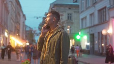 Portrait of handsome busy young adult man talking on phone standing outside looking at neon signs in city center. Beautiful African American male tourist communicating with smartphone.