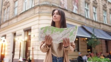 Portrait of young beautiful adventurous woman traveling standing in city center of Lviv holding map. Attractive happy female tourist looking at camera smiling planning routes for sightseeing.