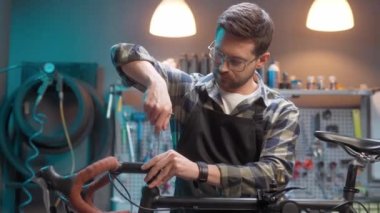 Beautiful busy focused caucasian man fixing bike with screwdriver at authentic garage. Attractive male craftsman doing hobby repairing bicycle with tools wearing glasses.