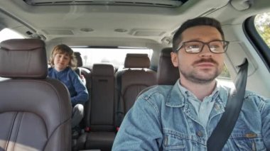 Portrait of attractive caring handsome young caucasian dad driving car with small cute son sitting in baby car seat smiling. Lovely family having trip together having fun talking. Car trip concept.