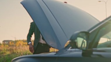 Attractive successful sad African American businessman opening hood of broken car looking at engine being depressed. Unhappy African male standing outside with broken vehicle on road.