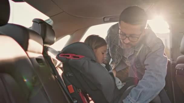 快乐英俊 负责任的父亲在家庭旅行前准备用安全带系住可爱的小女儿 金发可爱的小女孩笑着坐在婴儿车的座位上 — 图库视频影像