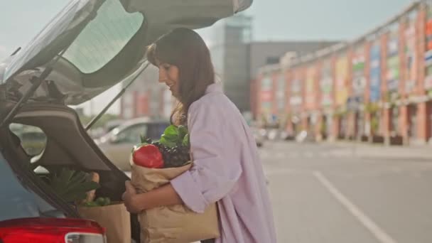 微笑的女孩拿着一袋蔬菜站在街上 雌性正在拿着苹果 把它放到相机里 拿着水果的小女孩摆姿势拍照 特写苹果的集中拍摄 — 图库视频影像